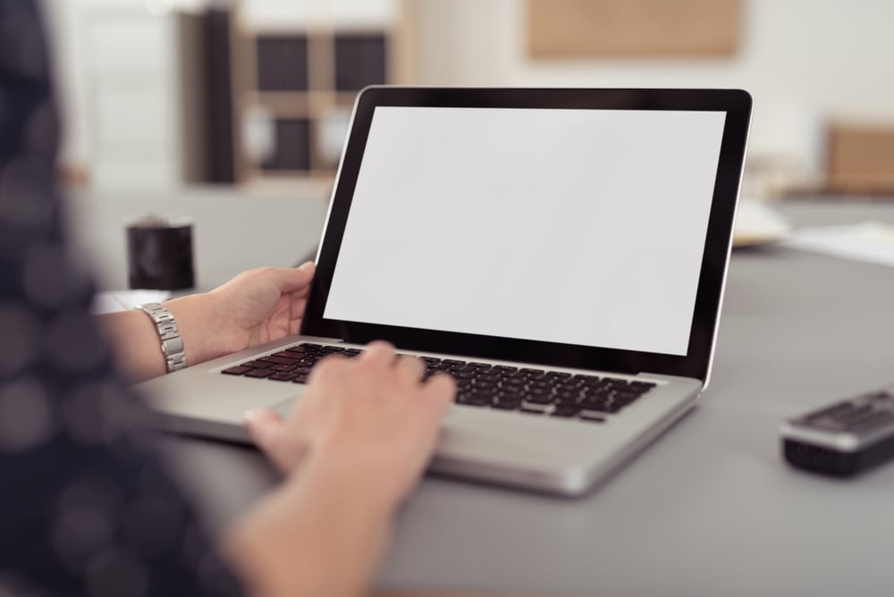 Businesswoman sitting at her desk navigating the internet on a laptop computer using the trackpad, over the shoulder view of great reporting and results by Favze.