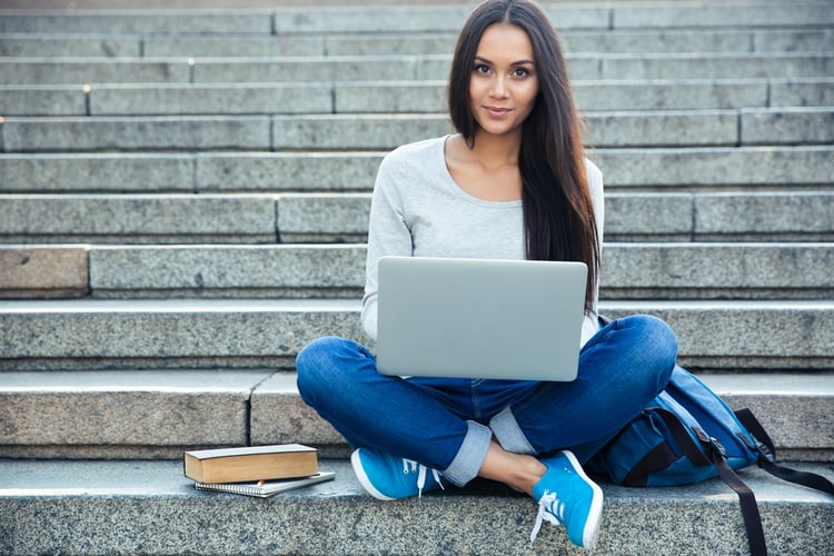 Happy young woman sitting on the city stairs and using laptop computer outdoors looking and getting great results by Favze.